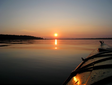 The sunrise is reflected off the hull of a kayak heading across Muskegon County's White Lake